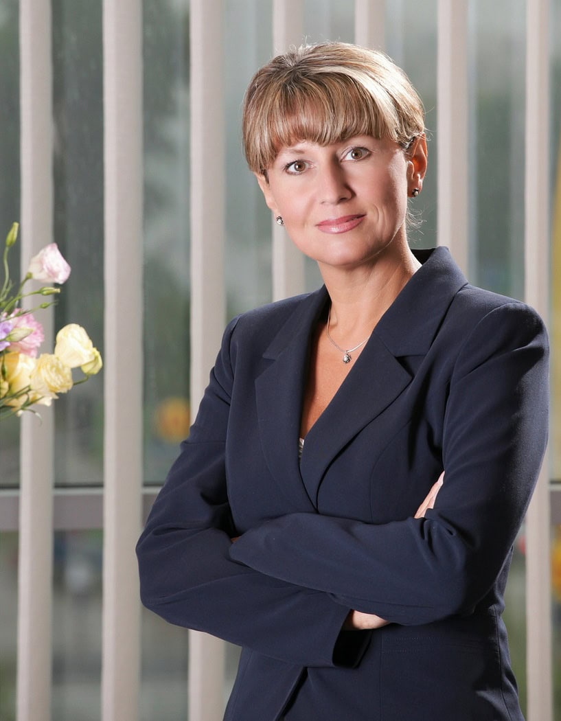 Elegant woman in professional suit standing confidently with arms crossed in front of modern glass building during daytime.